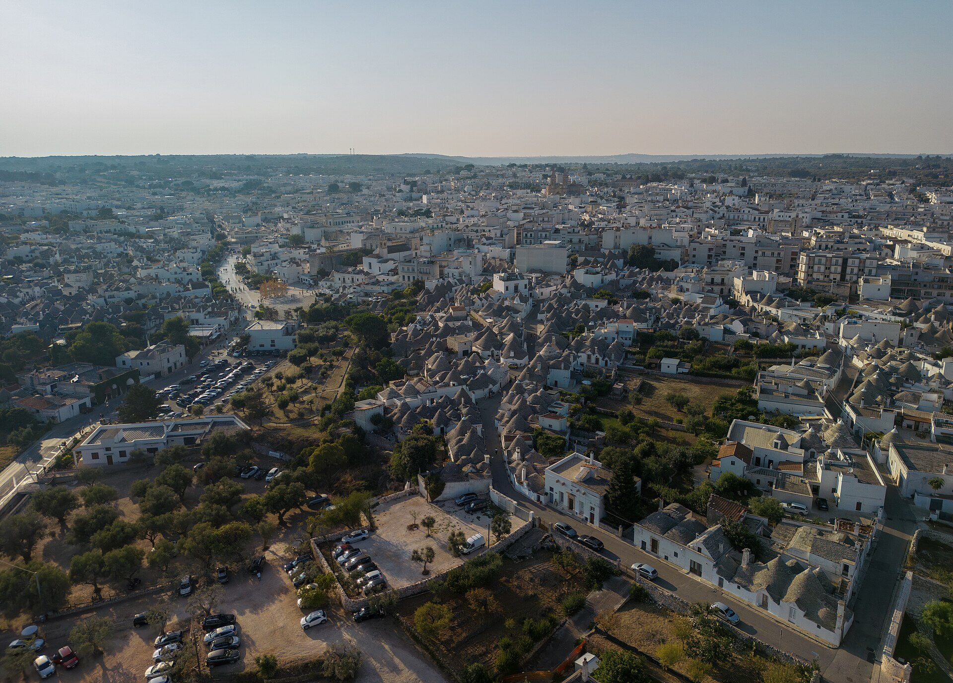 Ripresa aerea di Alberobello: quartiere dei trulli, parcheggi e tessuto urbano moderno.