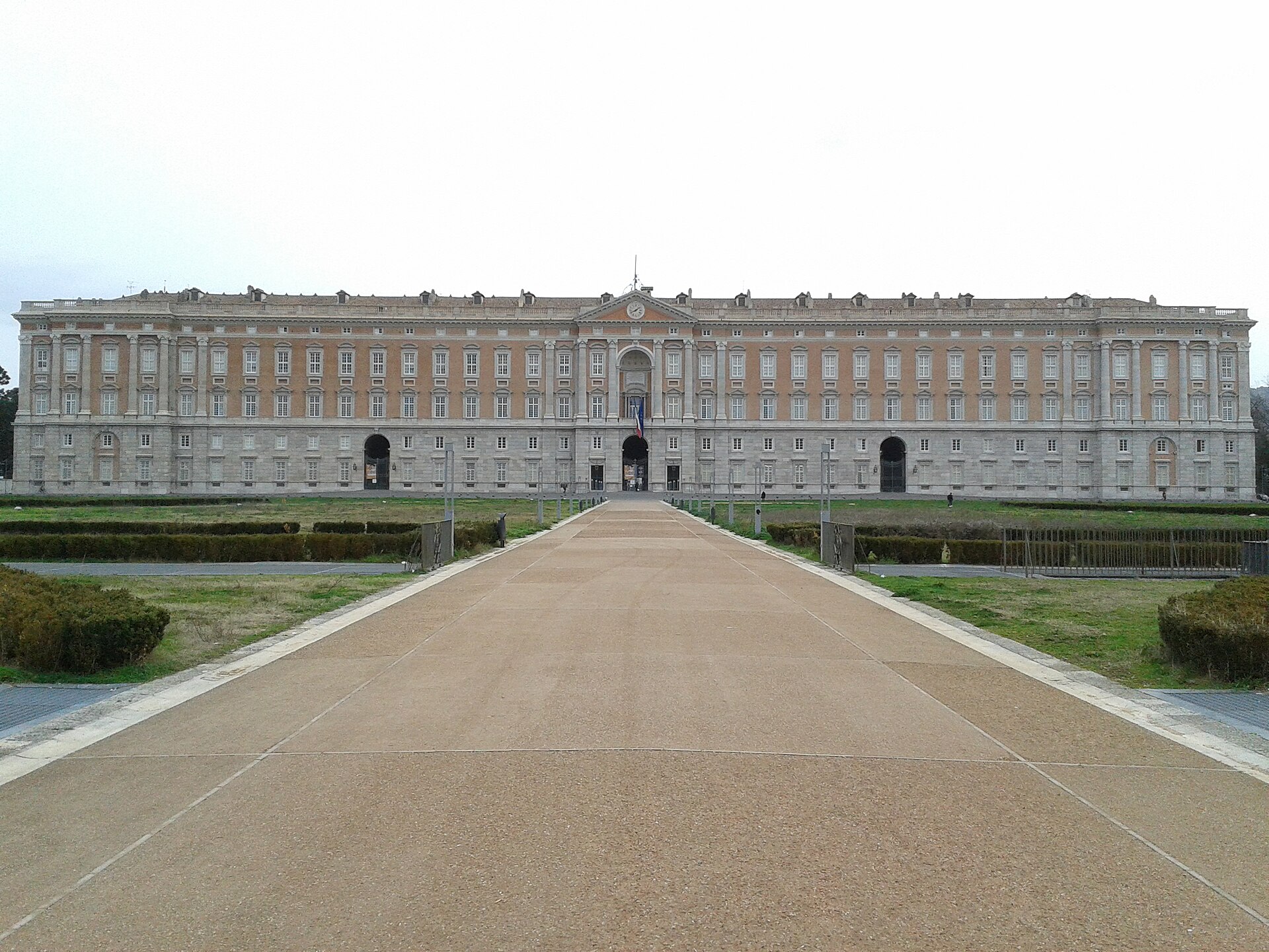 Facciata della Reggia di Caserta vista dal viale d’ingresso, palazzo di Vanvitelli sotto cielo coperto.